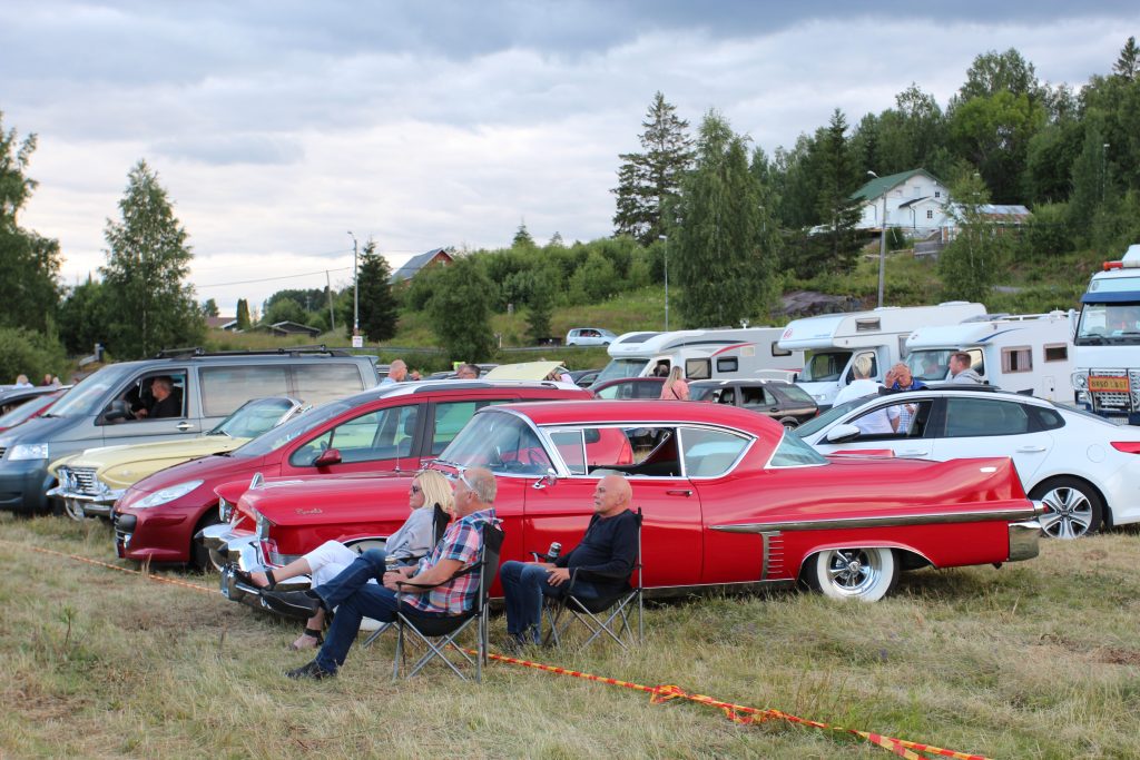 En rød og gammel amerikaner som var både lang og lav hadde parkert på den store parkeringsplassen.